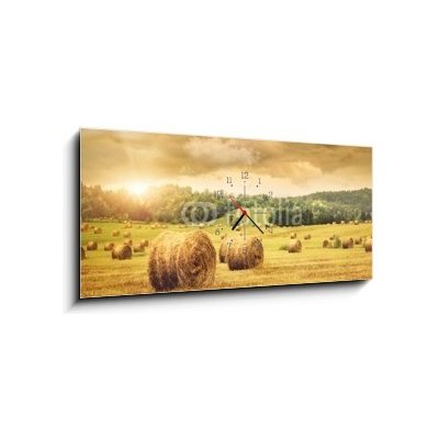 Obraz s hodinami 1D panorama - 120 x 50 cm - Field of freshly bales of hay with beautiful sunset Pole čerstvých balíků sena s krásným západem slunce