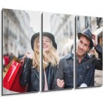 Obraz 3D třídílný - 105 x 70 cm - a trendy young couple wearing hats walking in the city in autum módní mladý pár nosí klobouky chůzi ve městě v podzimní – Sleviste.cz